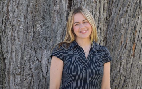 blond woman standing in front of a large tree trunk