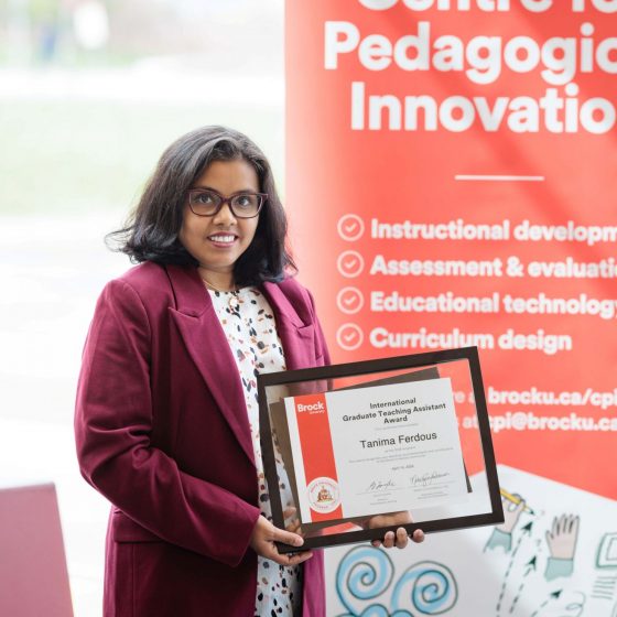 Tanima Ferdous smiles holding her International Graduate TA Award in front of the CPI banner