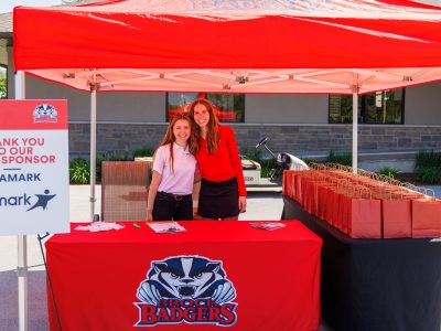 2 Brock Athletes posing at Brock Badgers branded git table outside golf course