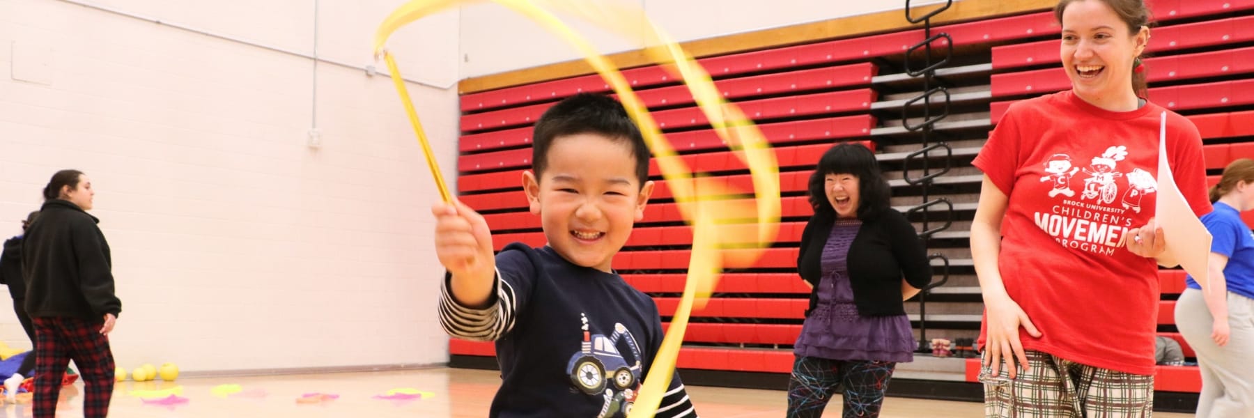 child spinning a ribbon while mom is laughing in background
