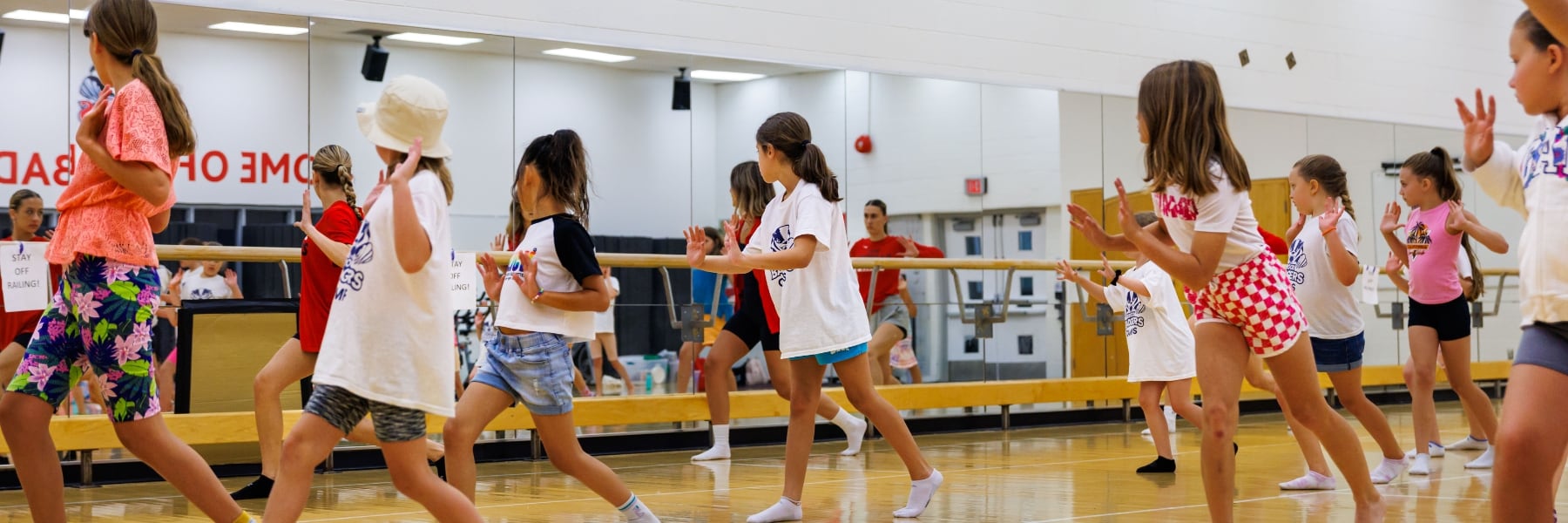 kids of various ages learning to dance in front of instructor and mirror