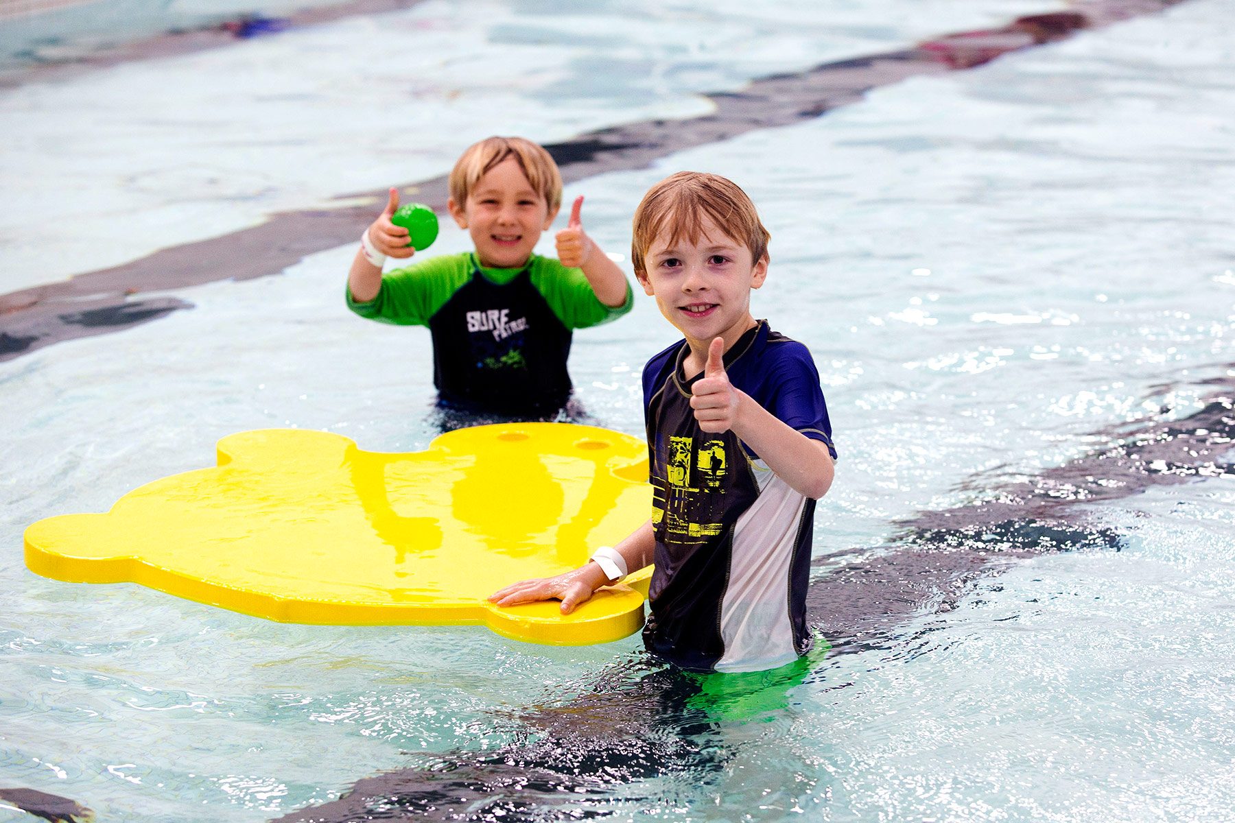 2 children in a pool with a float giving the thumbs up