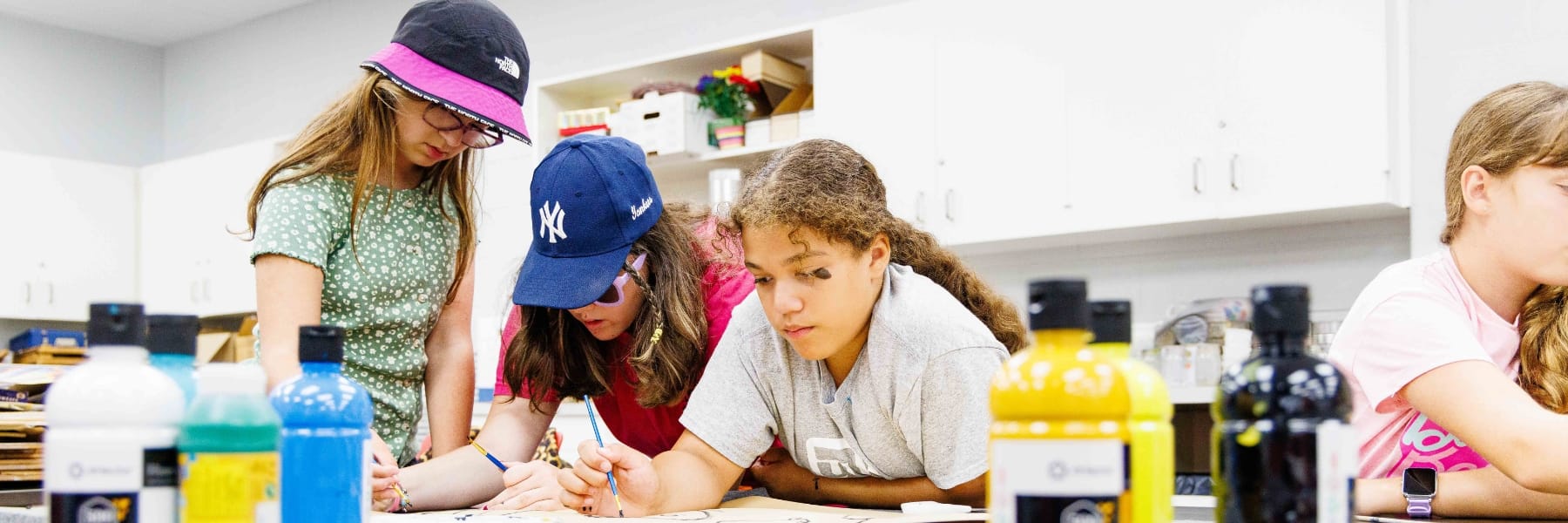 children doing art projects at a desk with paint and brushes
