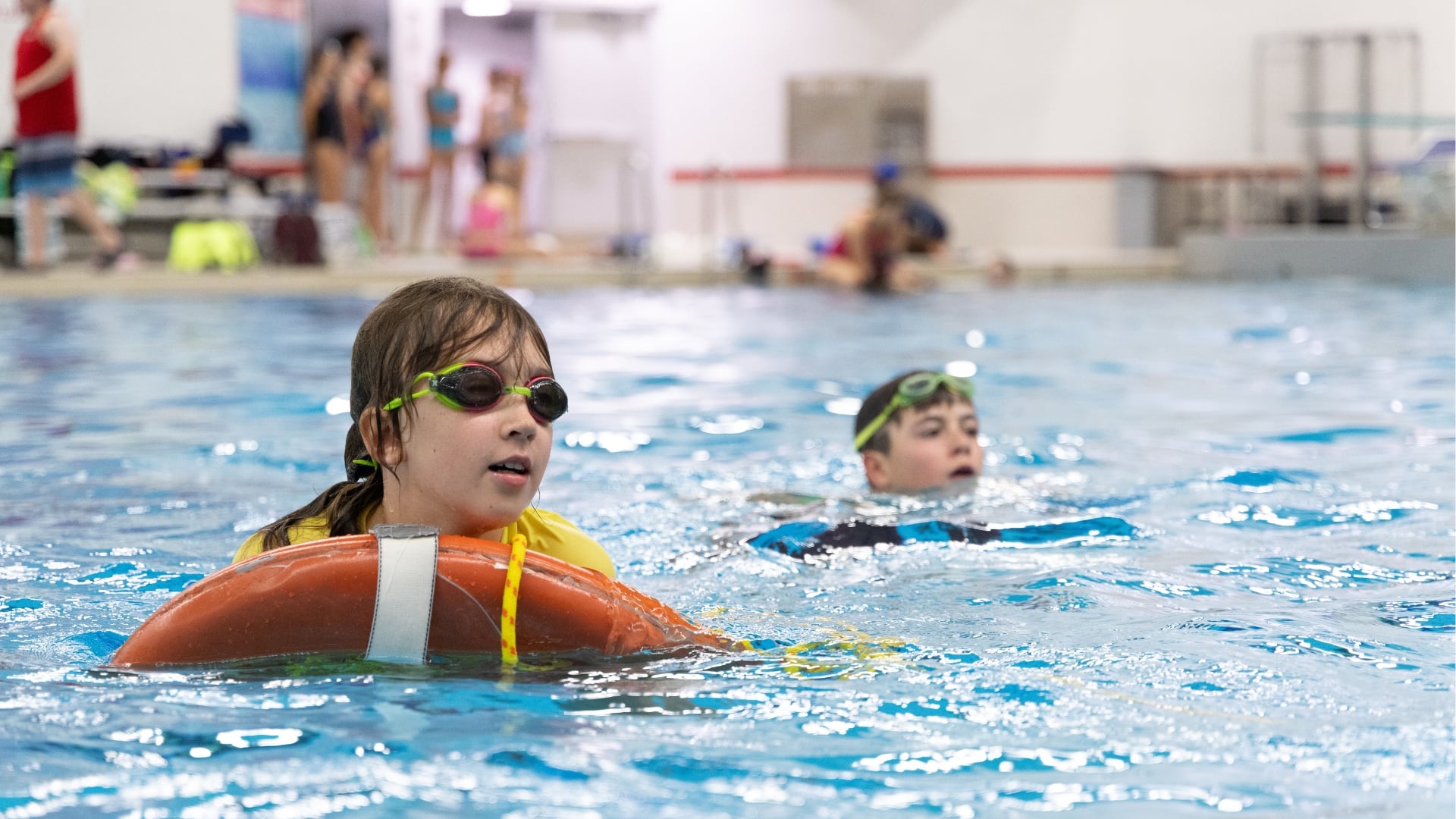 kids in pool one being towed in on a life ring 