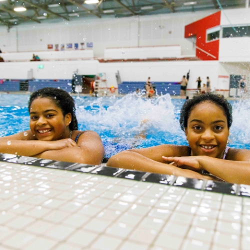 Swim-Lessons-500x500 two youth swimmers at edge of pool smiling