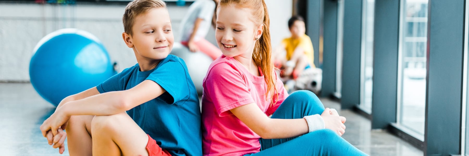 2 children smiling in a gym with an exercise ball
