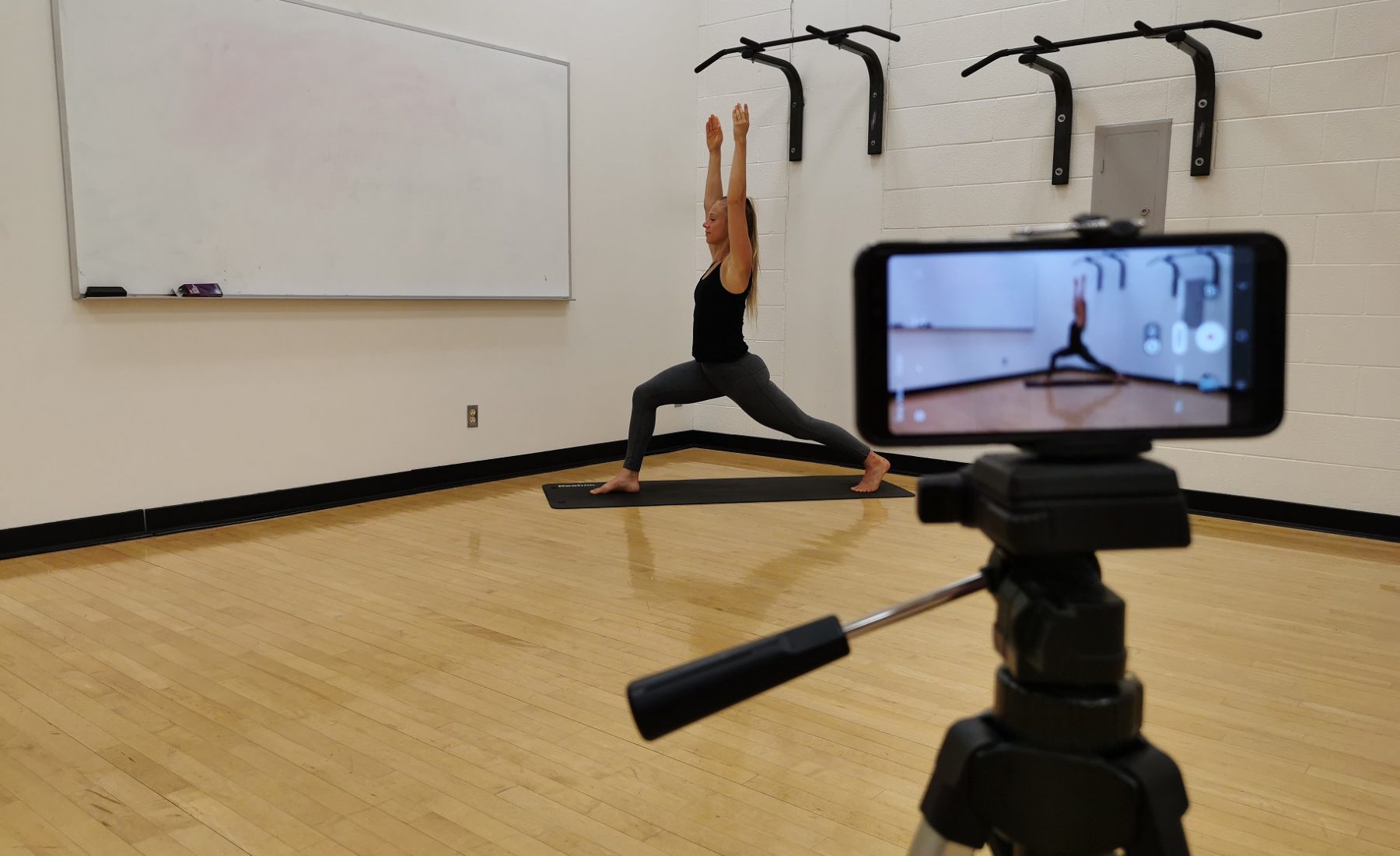 Person in fitness studio being filmed on a phone doing yoga 