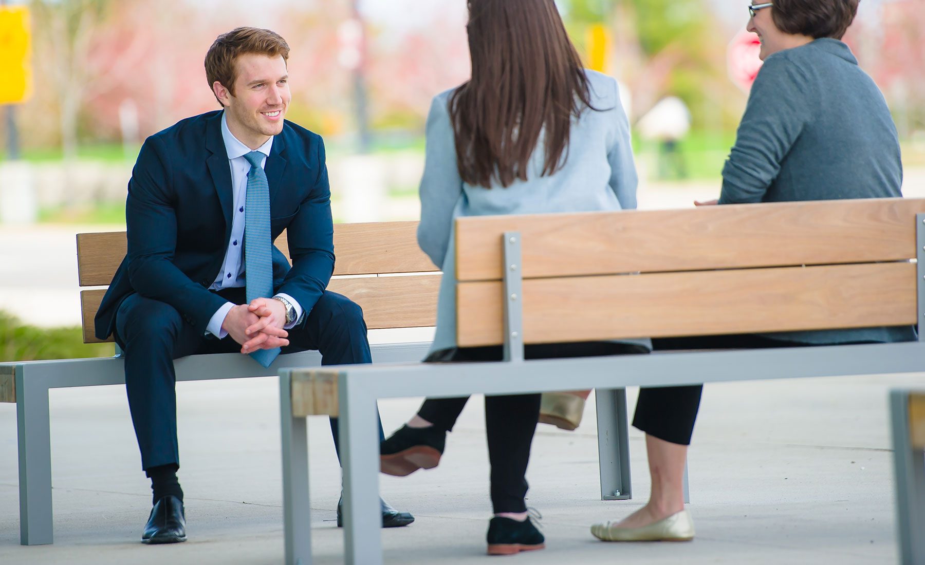 Three students dressed in business attire sitting out on benches 