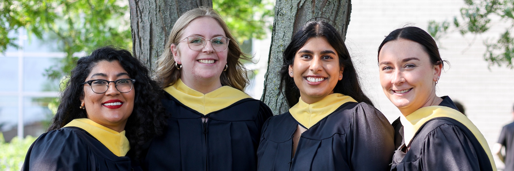 Four people in graduation robes standing together under a tree.
