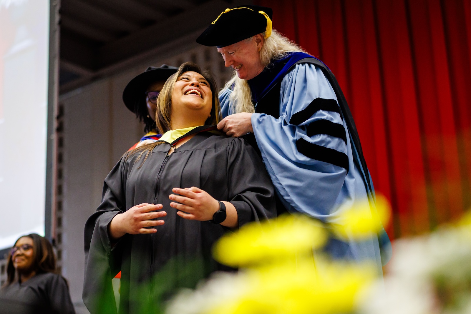 Two people in academic regalia on a stage.