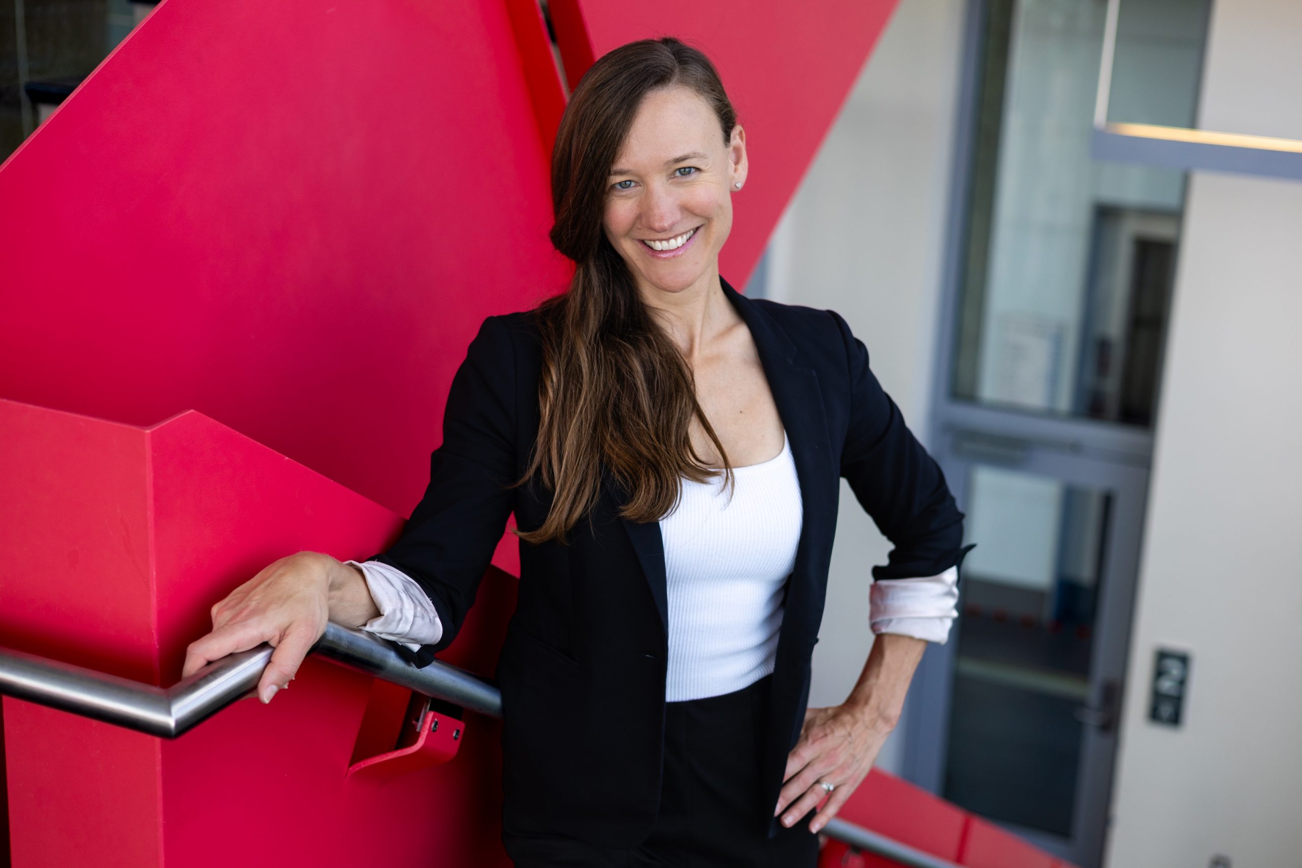Alison Cox standing against a red railing in a stairwell.