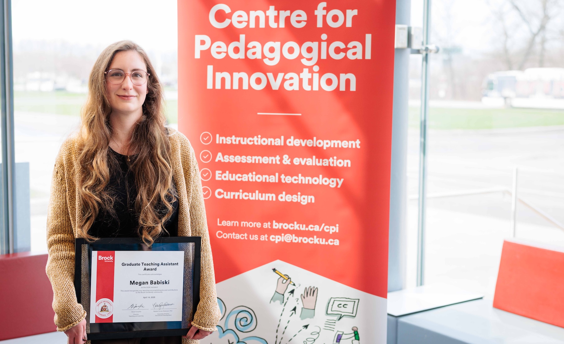 Megan Babiski holds her Graduate Teaching Assistant certificate next to a banner advertising Brock's Centre for Pedagogical Innovation.