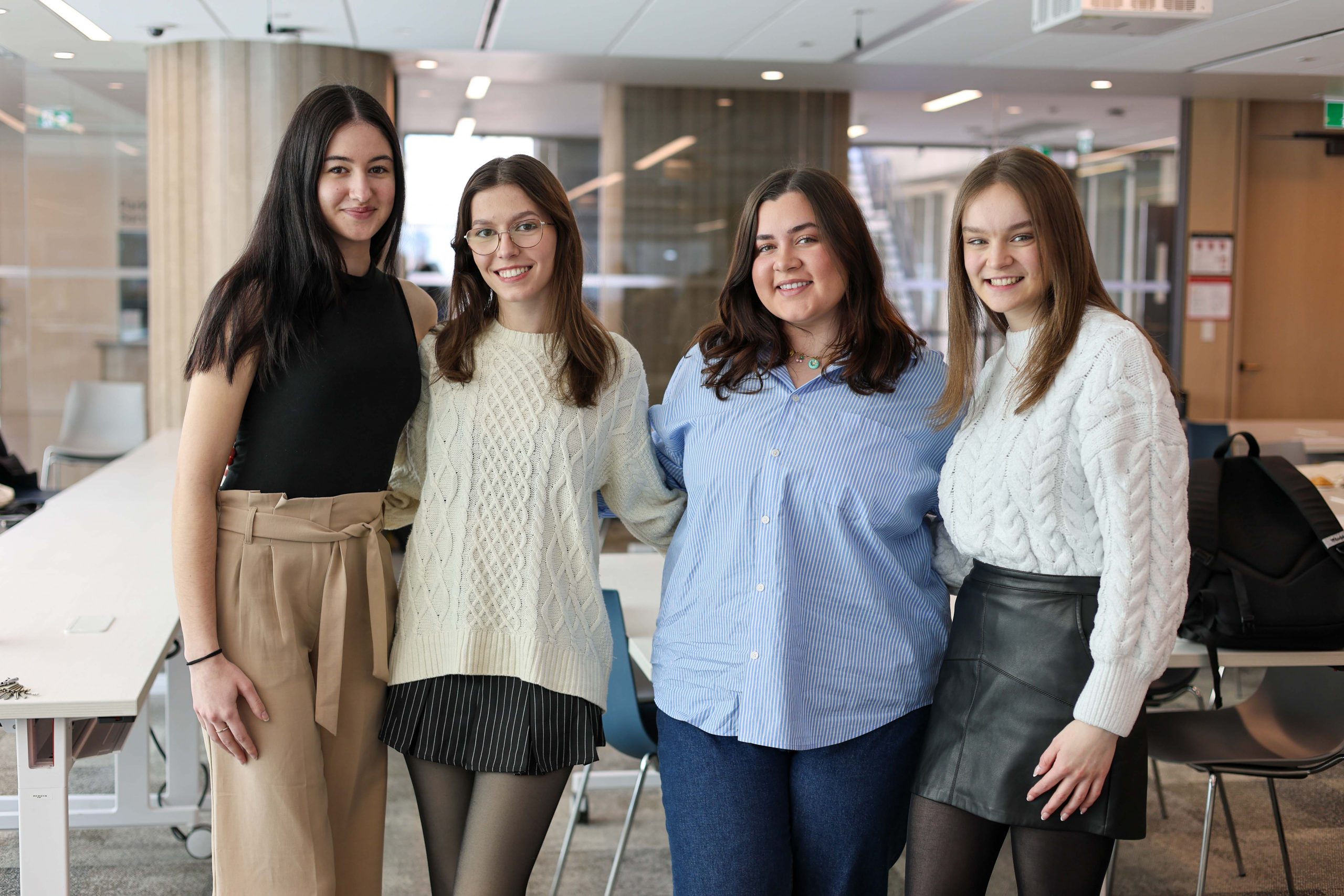 LING-edit6 Four students posing for a photo together in a room with floor to ceiling windows.