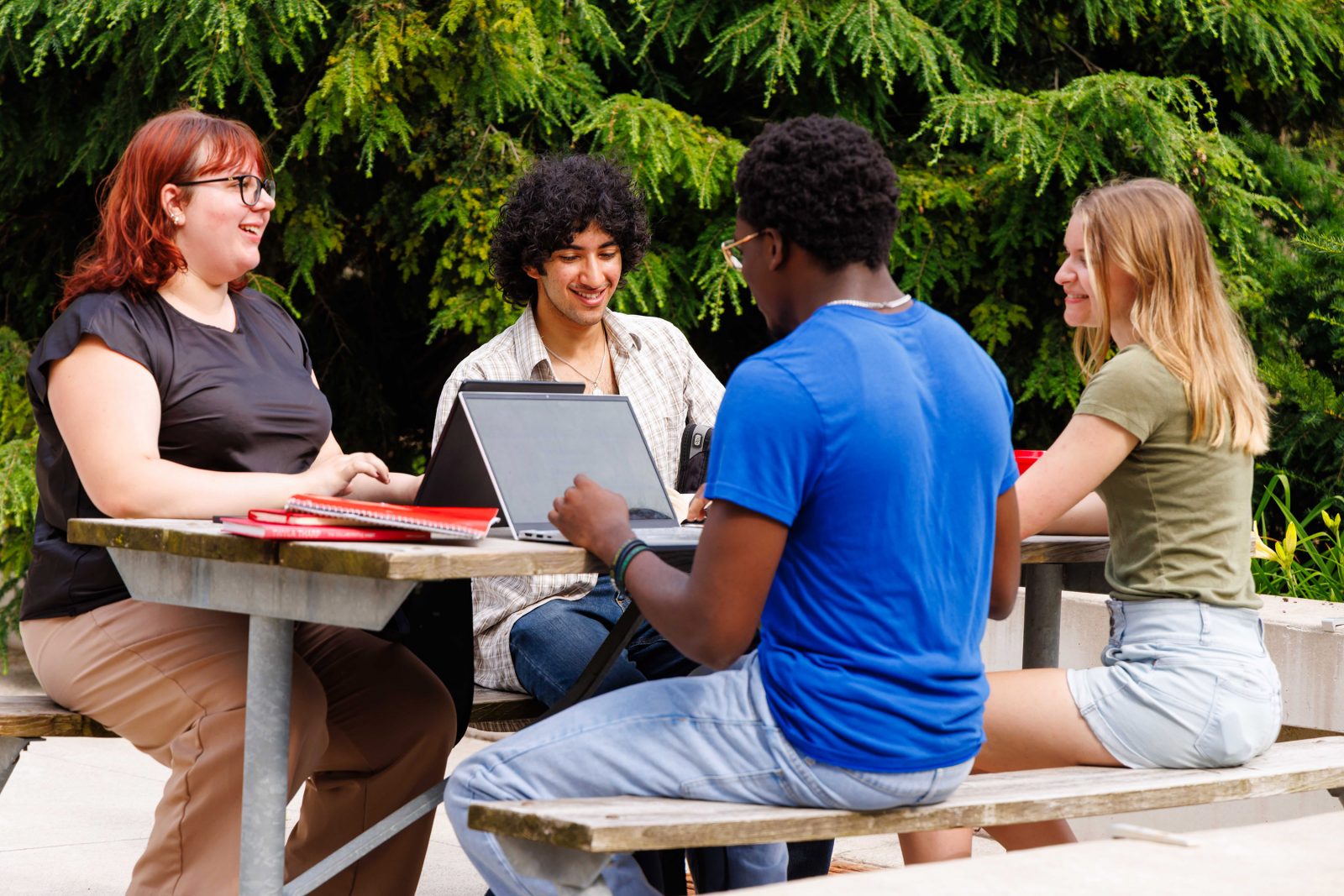 Four people sit at a picnic table talking to each other.