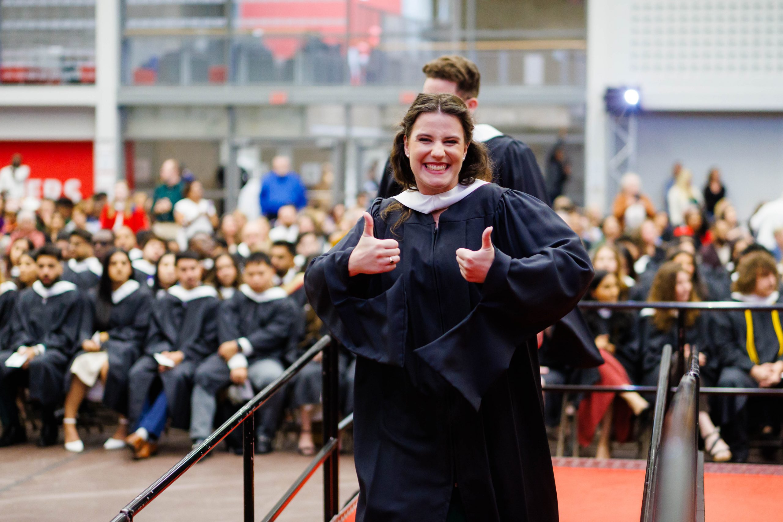 Erika Savage in academic regalia giving the thumbs up.