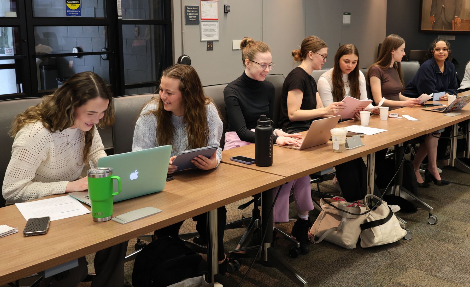 Group of university students sitting at tables with laptops. 