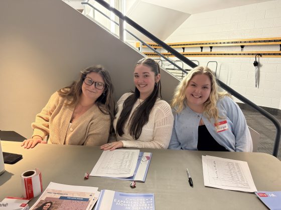 Three students sitting at a table with brochures and forms.