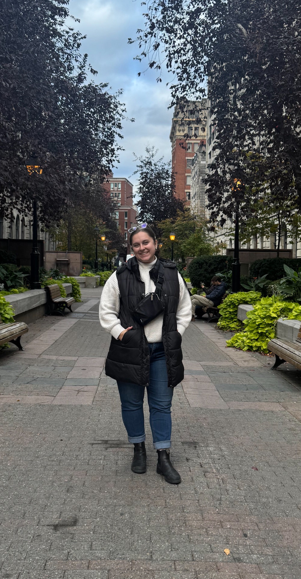 Emma Rupcic standing on a stone pathway with trees and buildings in the background.