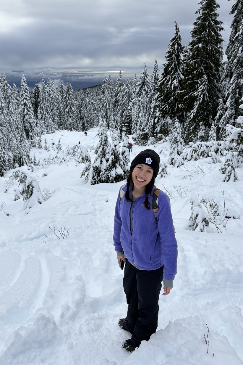 IMG_0300 Ava Hsieh standing on a snowy ski hill with trees in the background.