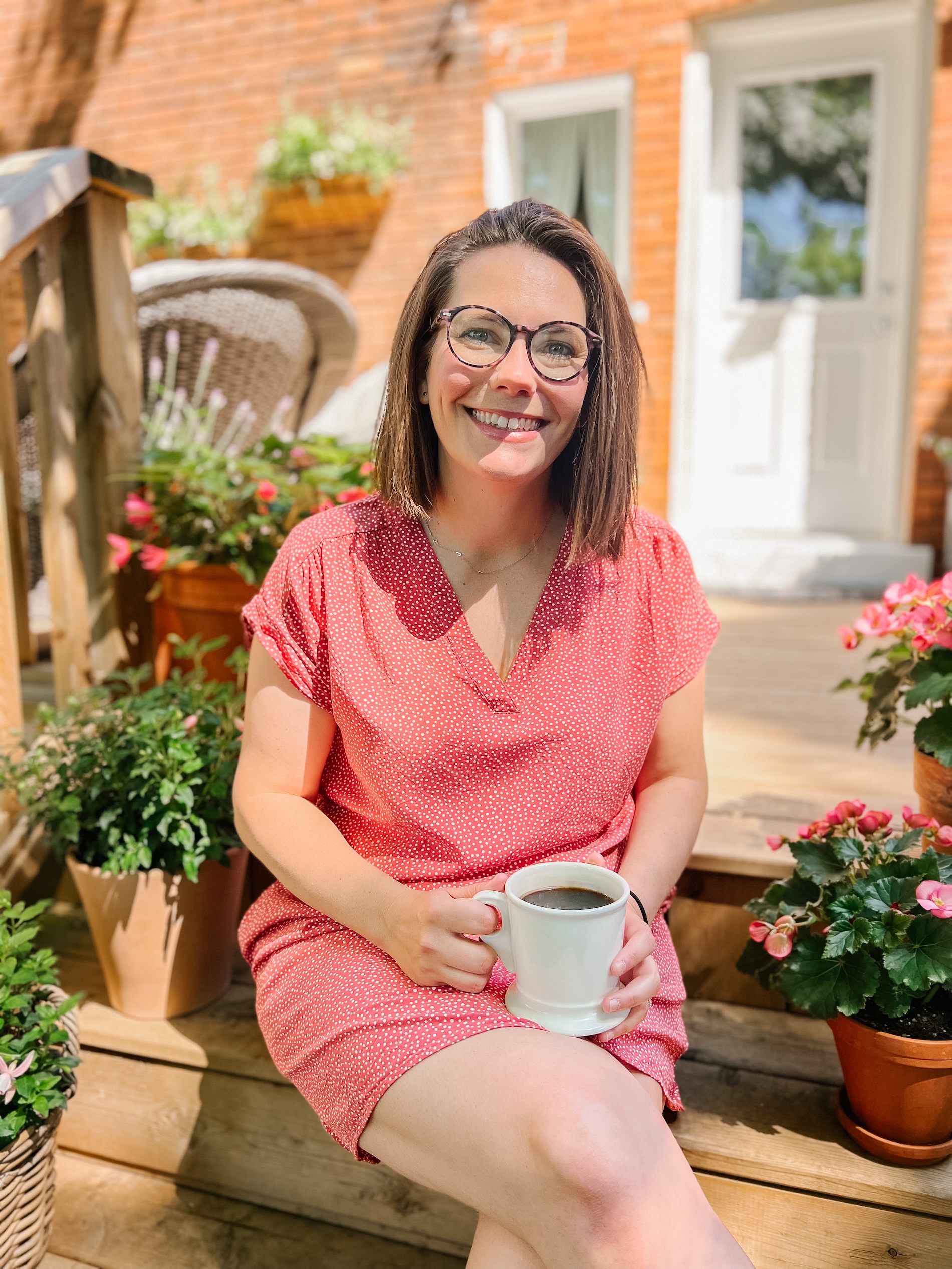 Teresa Hill sitting on a step in front of a house with a cup of coffee and potted plants stacked along the steps.