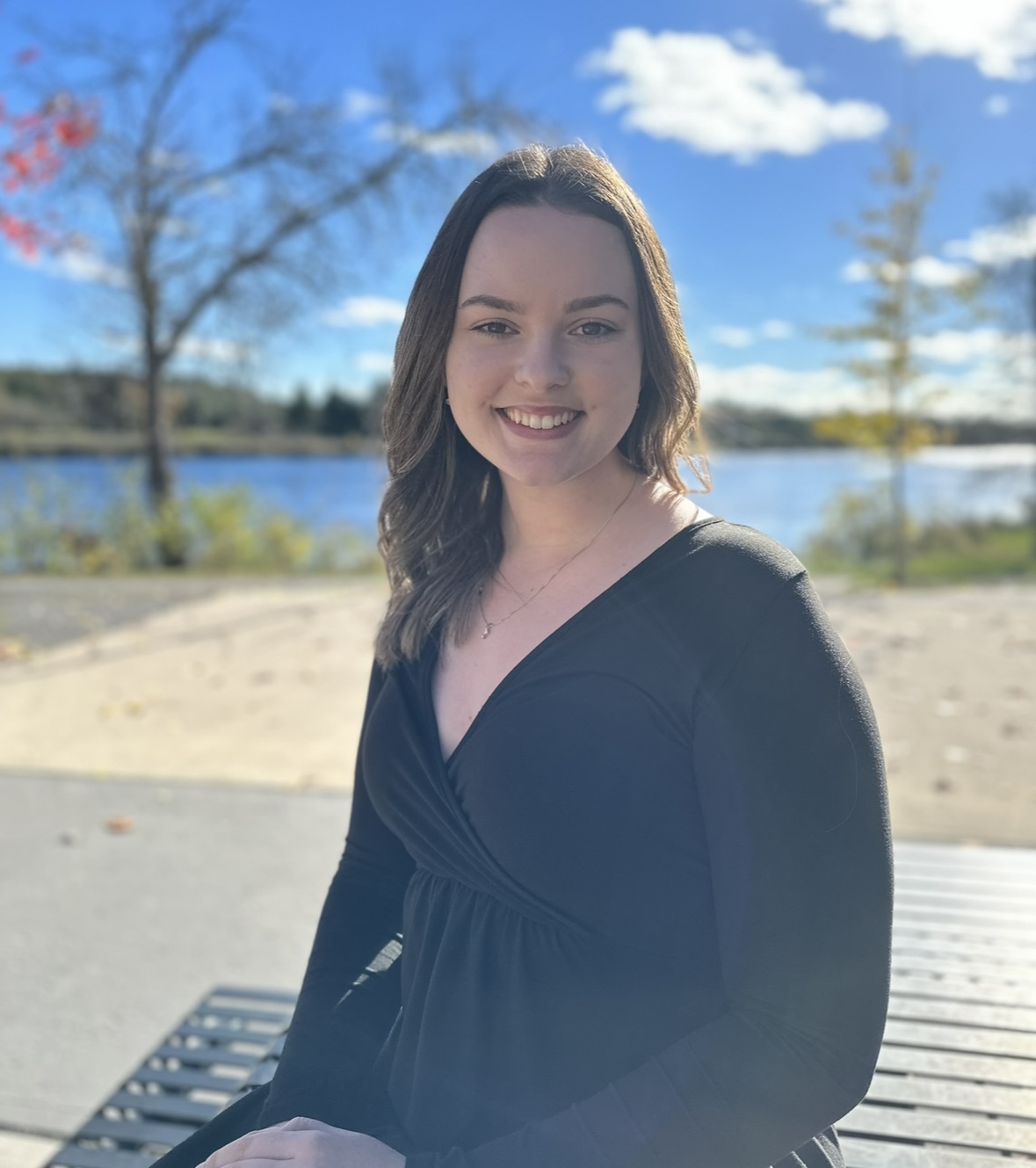 Sierra Sumner sitting on a bench with a view of trees and a lake in the background.
