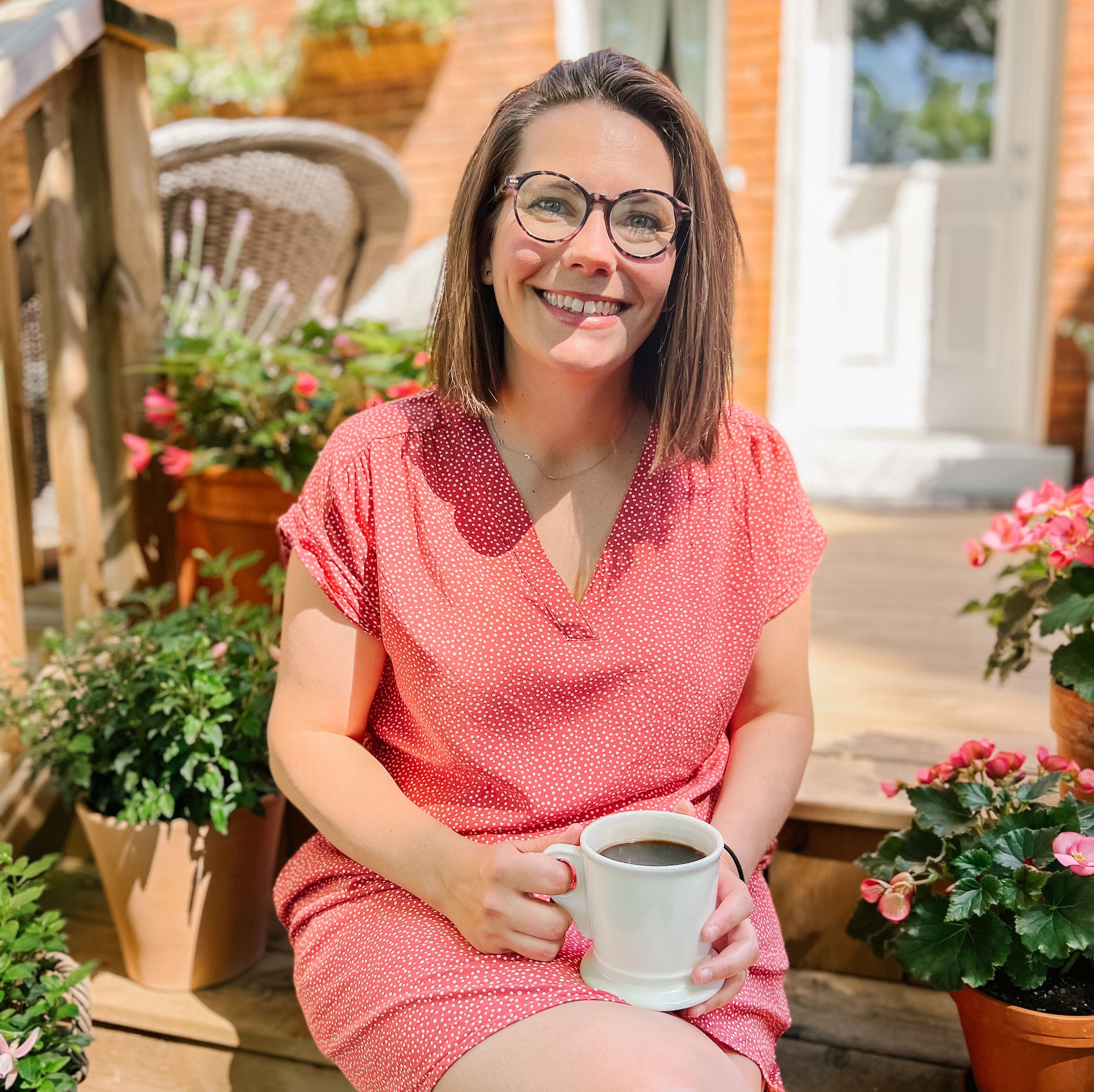 Teresa Hill sitting on a step in front of a house with a cup of coffee and potted plants stacked along the steps.