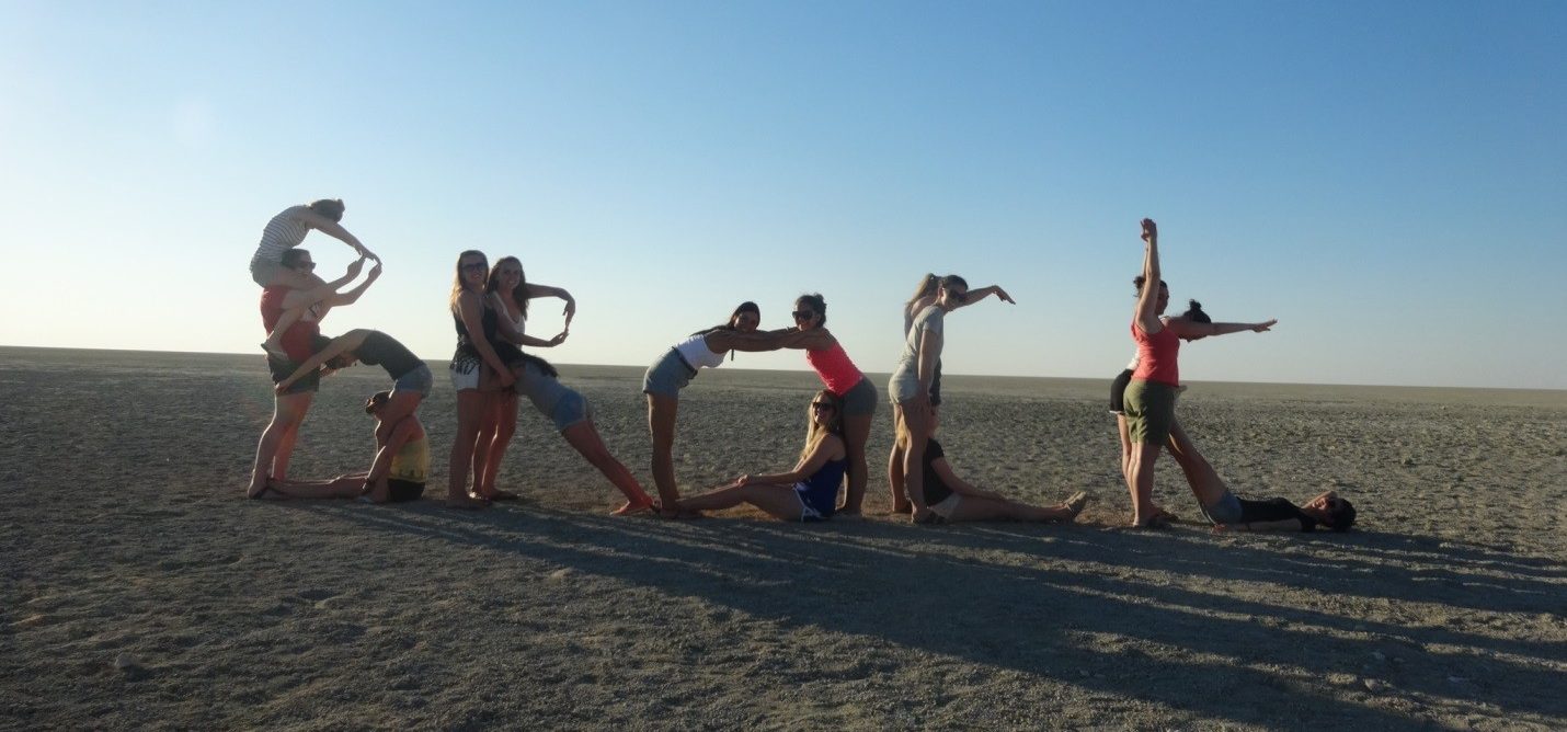 A group of students on a beach posing together in a way that spells out the word Brock.