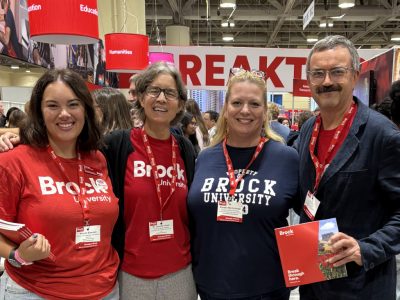 Four smiling people pose for a photo. They are wearing red lanyards and Brock University branded clothing
