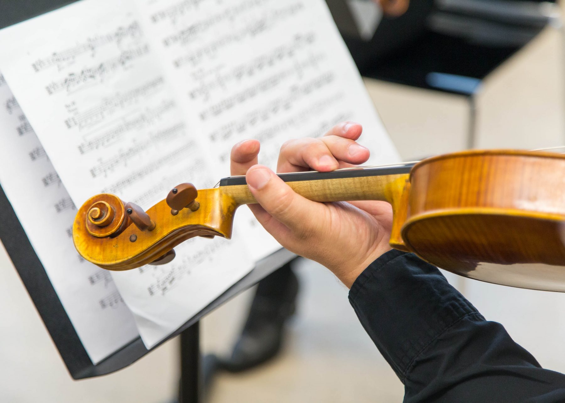 close up on hands playing a violin. Behind is some sheet music.