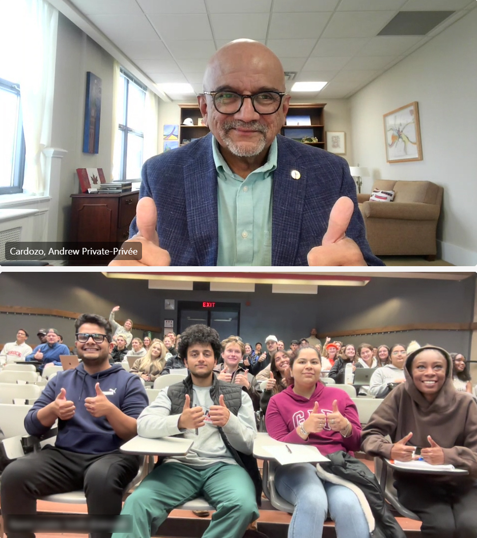 A screen shot from a virtual meeting. It is split with one half being the Senator in his office, and the other a class rom full of students in a lecture hall. everyone is giving a thumbs up.