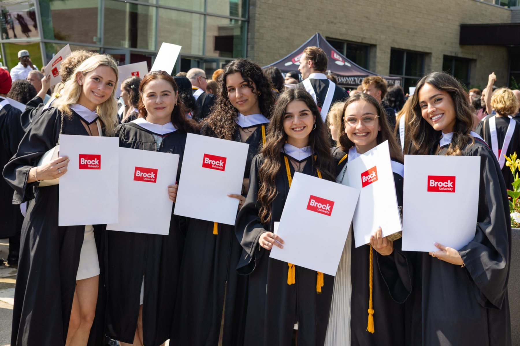 A group of graduates in their convocation gowns pose with their diplomas