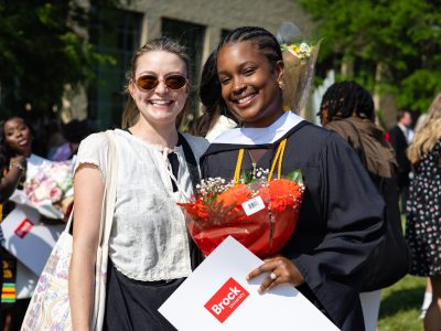 two people posing together for a photo. One is in their graduation gown.