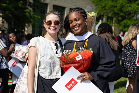 two people posing together for a photo. One is in their graduation gown.