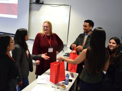 A group of people are talking and the event's MCs are holding red gift bags after the event has ended.
