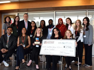 A group of 15 people stand together and pose for a photo. a few of the people in the front of the photo are holding a giant check and a trophy.
