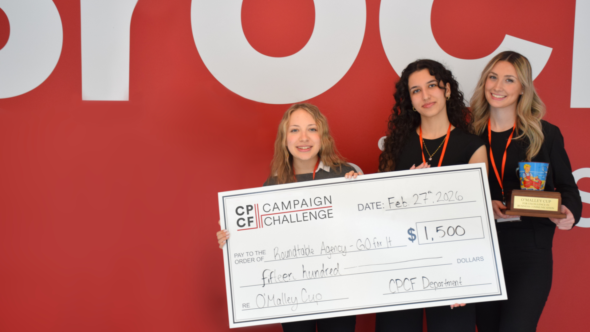 A group of three students pose for a photo with a giant check and regular sized trophy. 
