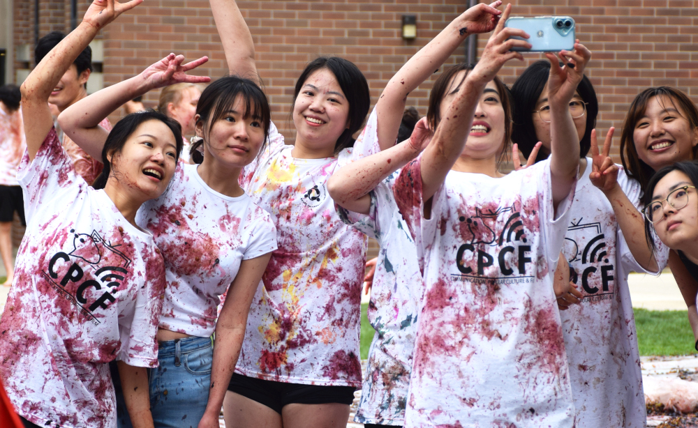 A group of students cluster together to take a selfie after they have participated in the Grape Stomp. Their once white "CPCF" t-shirts are stained with red and purple grape splotches.