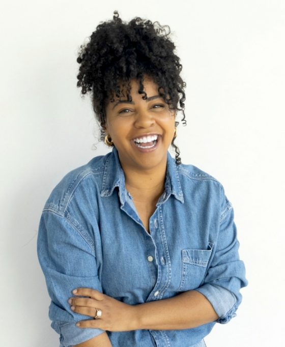 A smiling woman in denim stands in front of a white background