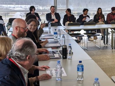 A group of people in business attire sit at tables in a conference room