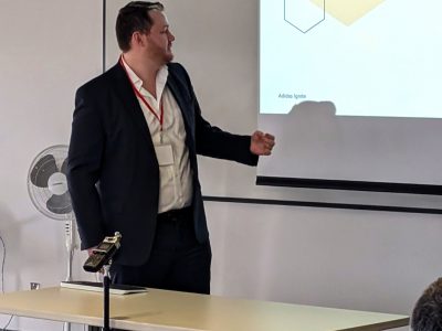 A student in business attire gestures as they give a presentation in front of a projector screen.