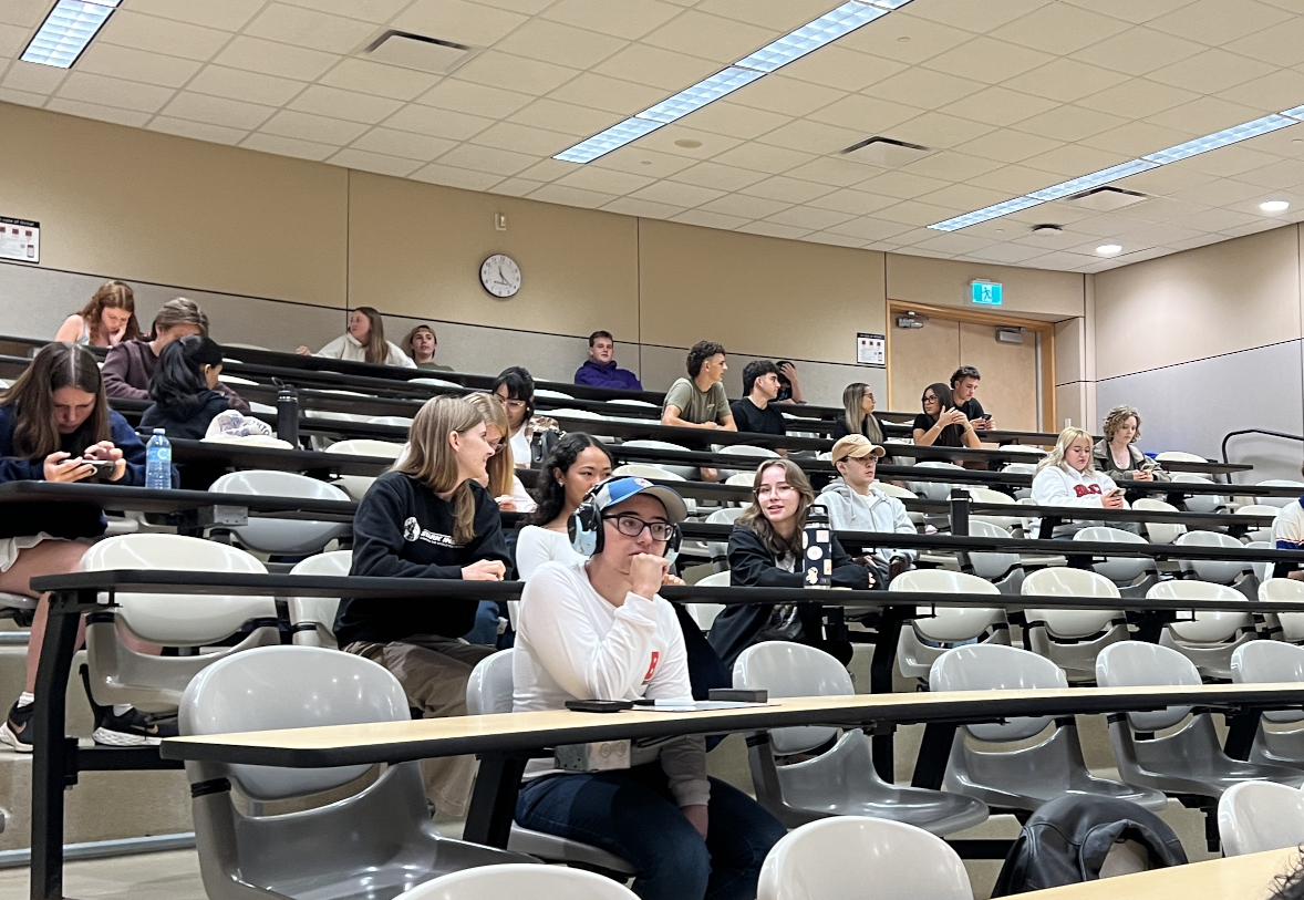 A group of students sitting in rows of desks in a tiered auditorium
