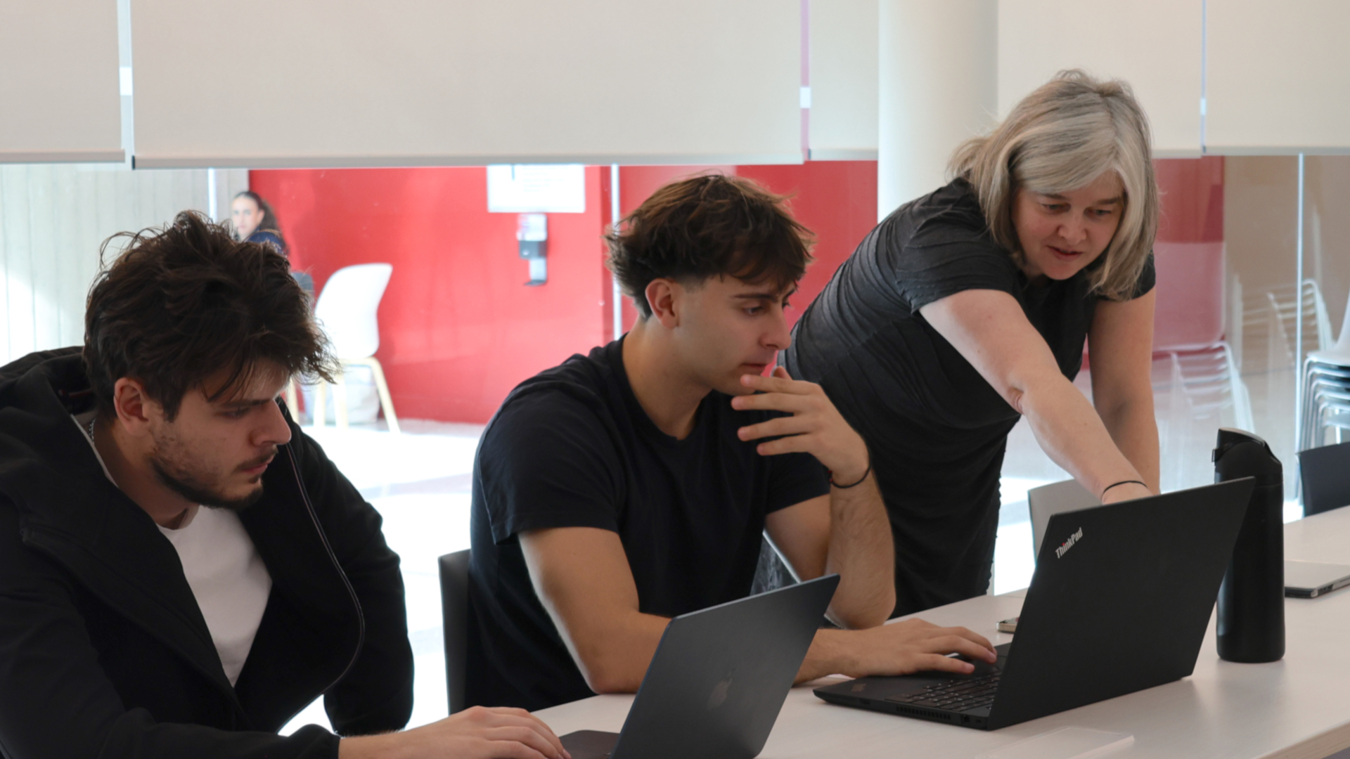 A professor points to a laptop while explaining something to two students 