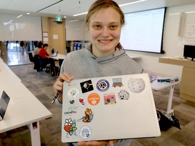 Wikipedia professional smiles and shows off their collection of stickers on their laptop.