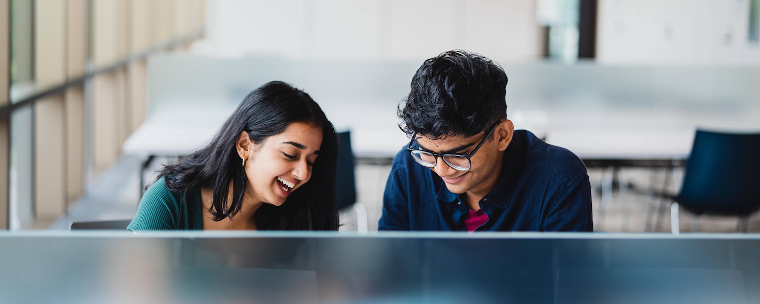 Two students laughing while studying in a lounge.