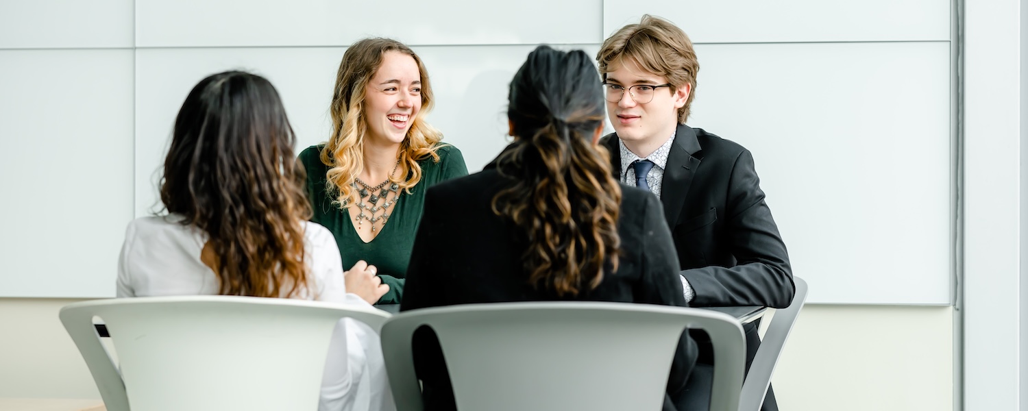Four students sit around a table talking and laughing.