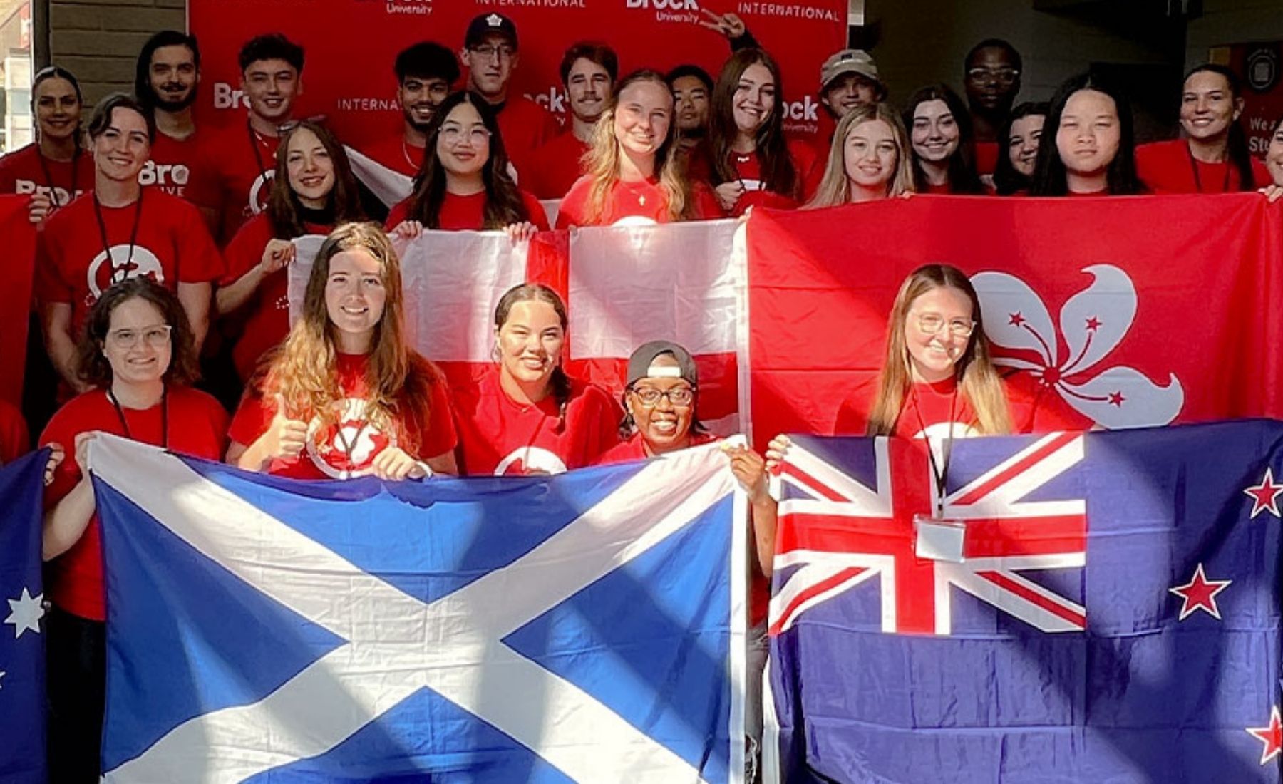 A group of students in Brock University red shirts holding up different national flags. 
