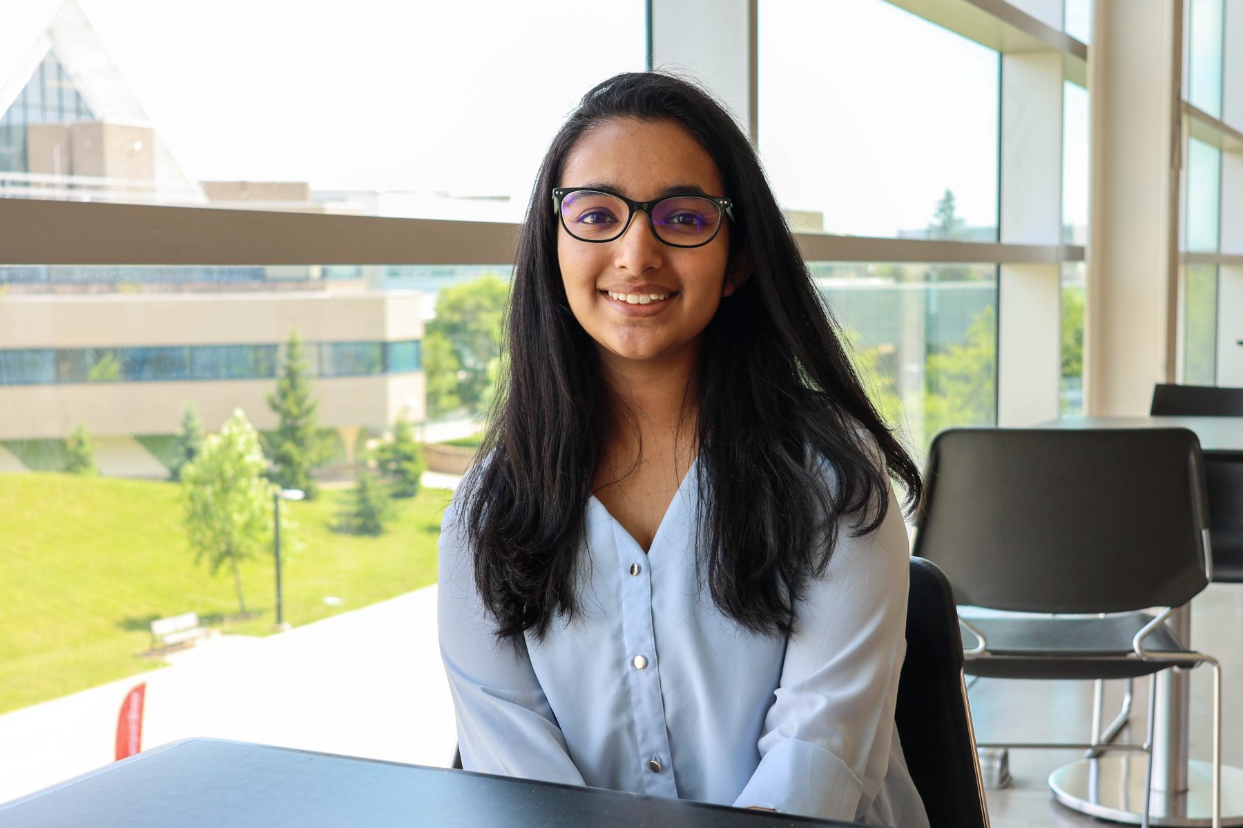 Mansi Vishwajitsinh Vansia sitting at a table with the Brock University campus seen through a window in the background.