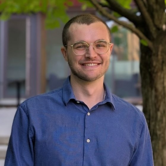 Noah Spencer standing in front of a building with trees.