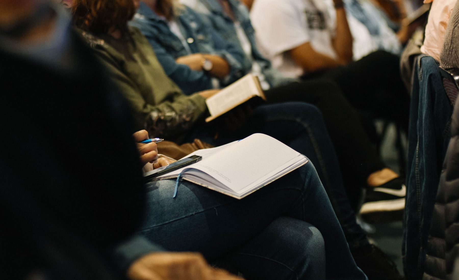 people in a group sit with notebooks open in an audience 