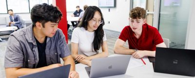 Three students sitting together and looking at their laptops.